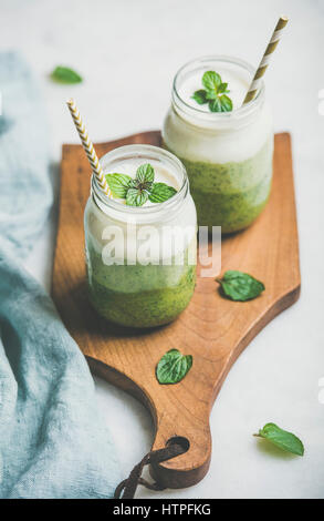 Ombre grüne Smoothies mit Minze im Glas mit einem Strohhalm auf Holzbrett über hellen grauen Hintergrund, selektiven Fokus geschichtet. Sauber, Essen, ve Stockfoto