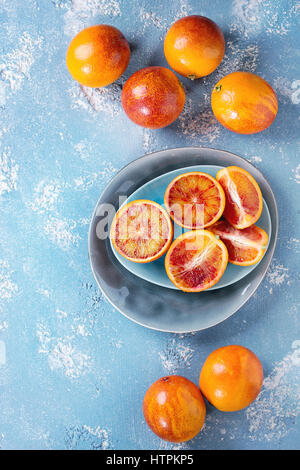 In Scheiben geschnitten und ganz reife saftige sizilianischen Blut Orangen Früchte auf Keramikplatte über blaue Betontextur Hintergrund. Ansicht von oben Stockfoto