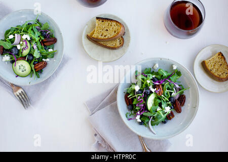 Schalen mit würzigen Pekannüsse-Feta-Rucola-Salat serviert mit Brot und Rotwein. Auf weißem Hintergrund fotografiert. Stockfoto