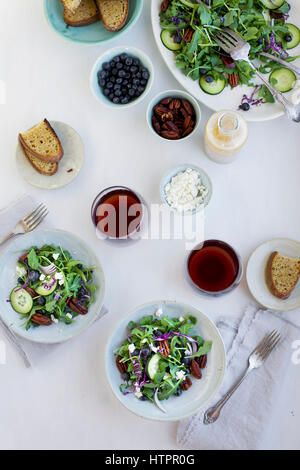 Schalen mit würzigen Pekannüsse-Feta-Rucola-Salat serviert mit Brot und Rotwein. Auf weißem Hintergrund fotografiert. Stockfoto