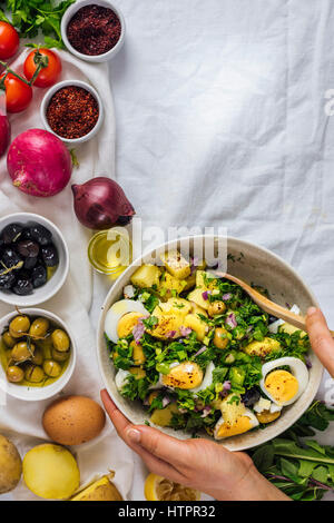 Eine Frau, die unter ständigem Rühren mediterranen Stil Kartoffelsalat mit Kräutern und hart gekochten Eiern, begleitet von schwarzen und grünen Oliven, roten Zwiebeln, Sumach und rote pepp Stockfoto