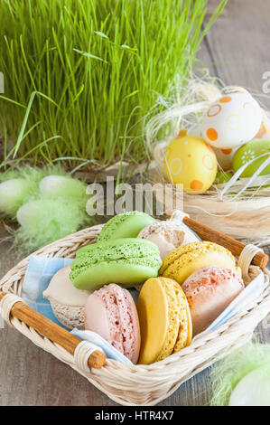bunten Baiser Makronen in einem Weidenkorb Ostern Eiern auf einem Rasen-Hintergrund für Ostern Stockfoto