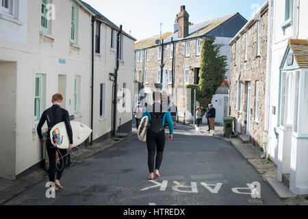 Teenager tragen Anzüge tragen Surf Boarder vorbei an Hütten in St. Ives, Cornwall, England. Stockfoto