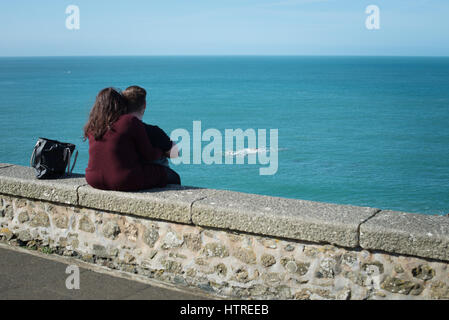 Ein paar Umarmung beim Sitzen auf einer Mauer aus Blick auf das Meer in St Ives, Cornwall, England, Großbritannien. Stockfoto