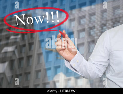 Hand des jungen Geschäftsmann schreiben Sie das Wort jetzt auf Wolkenkratzer Hintergrund, Konzept anwenden, um Ihr Geschäft zu fördern oder Präsentationen zu arbeiten. Stockfoto