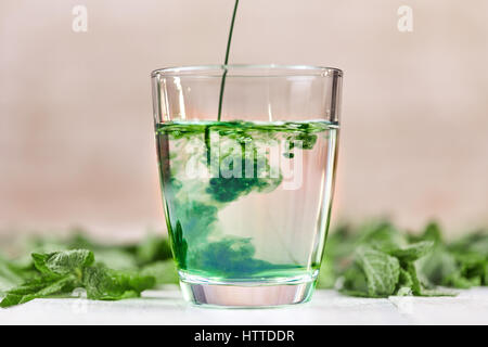 Auflösen von liquid Chlorophyll in Glas Wasser am weißen Tisch mit grüner Minze Stockfoto