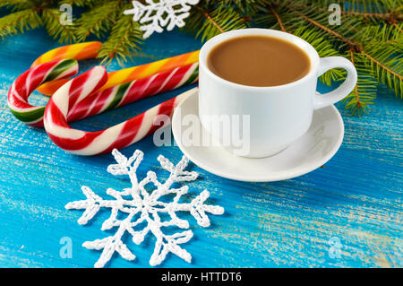 Thema Weihnachten. Eine Tasse Kaffee mit Milch (Cappuccino), in Form von hellen Zuckerstangen und grüne Fichte Zweige auf blauem Grund. Stockfoto