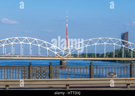 Eisenbahnbrücke über die Daugava Fluß (westliche Dwina) in Riga, der Hauptstadt von Lettland. Blick vom Steinbrücke mit Radio- und Fernsehturm auf backgound Stockfoto