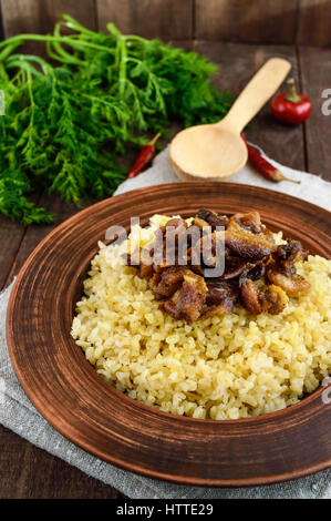 Östlichen traditionellen Weizen Brei - Bulgur mit gebratenen Stücke fettes Fleisch, Speck in einer Ton-Schale auf dunklem Holz. Stockfoto
