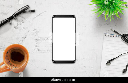 Schwarz Handy auf weißen Schreibtisch. Weißer Bildschirm Form Mockup isoliert. Modernes Display mit abgerundeten Ecken. Draufsicht der Schreibtisch mit Kaffee, Gläser, Pflanze. Stockfoto