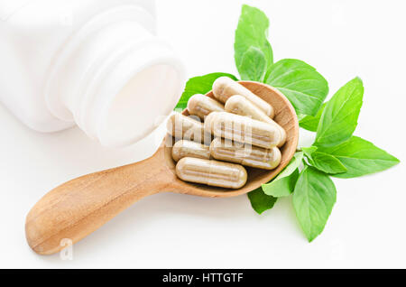 Kräutermedizin Kapseln in Holzlöffel mit grünen Blättern auf weißem Hintergrund. Stockfoto