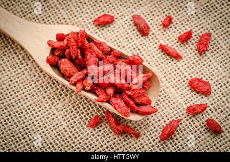 Roten getrockneten Goji-Beeren in Holzlöffel auf Sack Hintergrund. Stockfoto