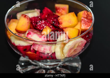 Obstsalat auf dunklem Hintergrund, Pfirsiche, Bananen, Drachenfrucht Stockfoto