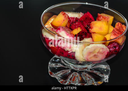 Obstsalat auf dunklem Hintergrund, Pfirsiche, Bananen, Drachenfrucht Stockfoto