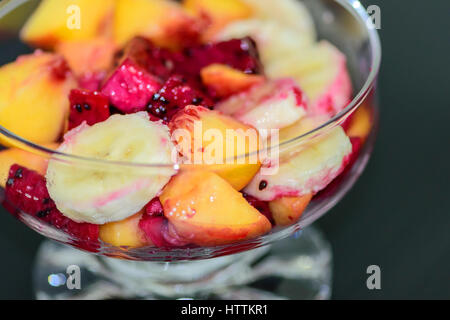 Obstsalat auf dunklem Hintergrund, Pfirsiche, Bananen, Drachenfrucht Stockfoto