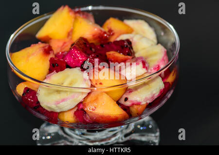 Obstsalat auf dunklem Hintergrund, Pfirsiche, Bananen, Drachenfrucht Stockfoto