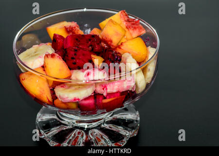 Obstsalat auf dunklem Hintergrund, Pfirsiche, Bananen, Drachenfrucht Stockfoto