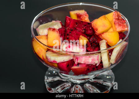 Obstsalat auf dunklem Hintergrund, Pfirsiche, Bananen, Drachenfrucht Stockfoto