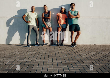 Voller Länge Schuss von jungen Freunden zusammen posieren. Gruppe von Fitness-Menschen, die von einer Mauer im Freien stehen. Stockfoto