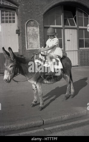 kleines Mädchen im Sonntagsstaat Kleidung sitzt auf einem kleinen Esel, eine Tradition seit den 1880er Jahren, England der 1920er Jahre. Stockfoto