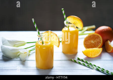 Frisch gepresster Orangensaft in das Glas mit Stroh und Calla auf weißer Holztisch. Vertikale erschossen Stockfoto