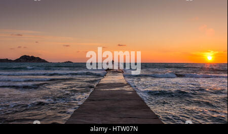 Einsamer Mann am Ende des Piers mit Wellen, die auf ihn bei Sonnenuntergang. Korfu Griechenland Stockfoto