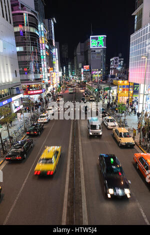 TOKYO, JAPAN - ca. April 2013: Fahrzeuge fahren auf der Straße. Beleuchtete Werbung Banner sind an Gebäudefassaden. Das Nachtleben ist auf den Straßen von Shinju Stockfoto