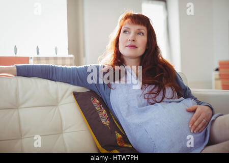 Nachdenkliche schwangere Frau im Wohnzimmer entspannen Stockfoto