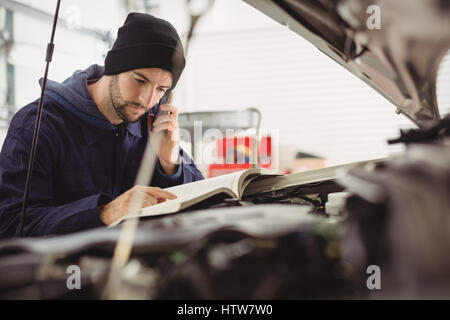 Mechaniker, die Bedienungsanleitung zu lesen, während des Gesprächs auf dem Handy Stockfoto