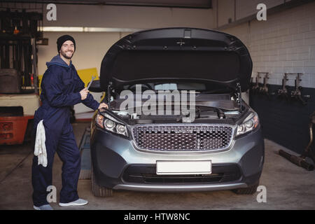 Mechaniker lächelnd und halten eines Schraubenschlüssel-Werkzeugs in garage Stockfoto