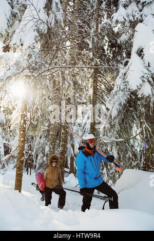 Paar mit Ski und Snowboard zu Fuß auf verschneiten Bergen Stockfoto