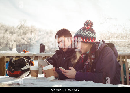 Hochzeitspaar Skifahrer am Tisch sitzend und mit Handy und digitale Tablett Stockfoto