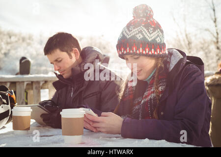 Glücklich Skifahrer paar mit Handy und digitale Tablett am Tisch Stockfoto