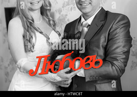 Schwarze Katze und Wort Liebe auf Russisch in Händen der Braut und des Bräutigams, schwarz-weiß-Bild mit roter Aufschrift Stockfoto