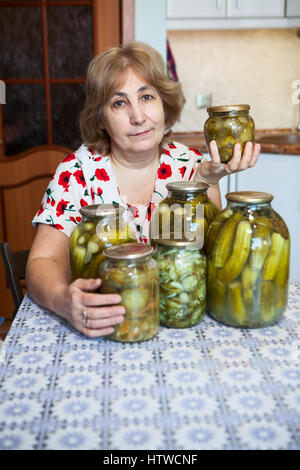Kaukasischer Frau mittleren Alters sitzt an einem Tisch mit Glasgläser voller gesalzene Gurken Stockfoto