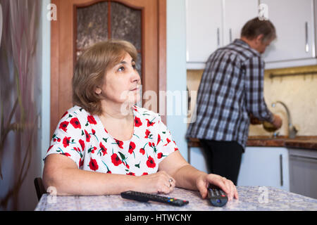 Kaukasische Frau sieht fern und Pausen, Mann hilft in der Küche - wäscht Gerichte Stockfoto