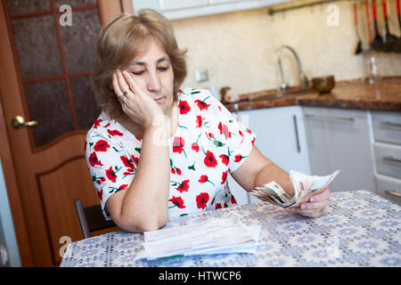 Kaukasische Frau sieht mit traurig über Quittungen für kommunale Zahlung beim Sitzen auf der Küche Stockfoto