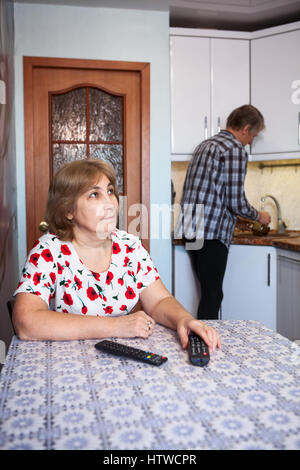 Kaukasische paar, Mann hilft in der Küche, wäscht Gerichte, die Frau ist vor dem Fernseher Stockfoto