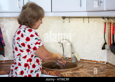 Kaukasische senior Frau Glas im Spülbecken waschen Stockfoto