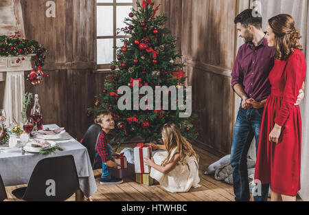 Lächelnden Eltern betrachten Kinder öffnen Geschenk-Boxen in der Nähe von Christmas tree Stockfoto