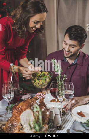 Junge Frau, die Platte für ihren Ehemann Rosenkohl aufsetzen Stockfoto