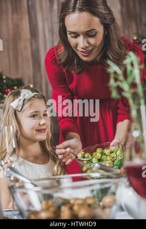 Junge Frau, die Platte für die Tochter Rosenkohl aufsetzen Stockfoto