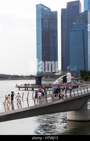 Menschen zu Fuß über die Jubilee Bridge, Merlion spritzenden Wasser in die Marina Bay und Finanzzentrum Marina Bay im Hintergrund. Stockfoto