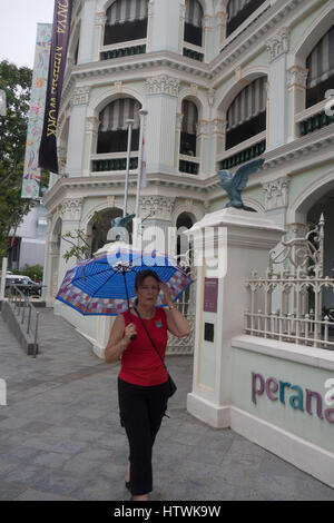 Eine Kaukasische Frau mit einem Regenschirm zu Fuß vor der Peranakan Museum, Singapur. Stockfoto