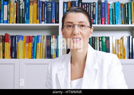 Reife Frau in weißen Blazerin vor Bücher erklären etwas, Professor, Lehrer, Hauslehrer, Trainer, Berater, Berater, Therapeut Stockfoto