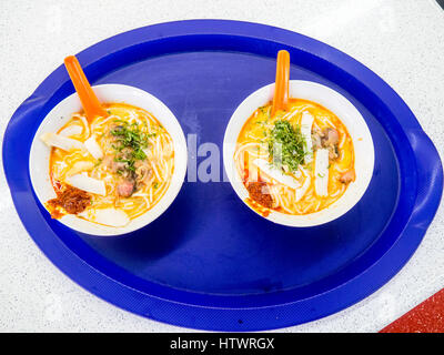 Zwei Schüsseln mit Curry Laksa Suppe, ein traditionelles Nyonya Gericht auf einem blauen Plastikbehälter. Stockfoto