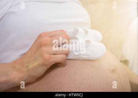 Kleine Schuhe für das ungeborene Kind in den Bauch der schwangeren Frau Stockfoto