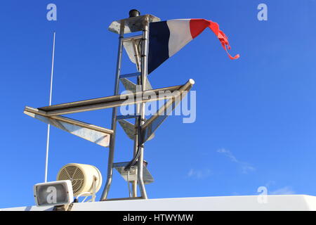 Navigational und Sicherheitsausrüstung auf einem mediterranen Schiff unter der Flagge des französischen Tricoleur gegen einen klaren blauen Himmel Stockfoto