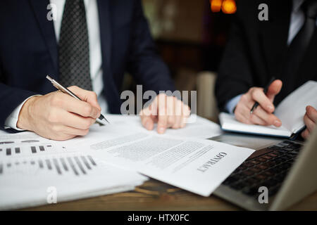 Closeup Portrait von zwei unkenntlich Geschäftsleute tragen schwarze formalen Anzüge Unterzeichnung Vertrag Papiere am Tisch während der Sitzung Stockfoto