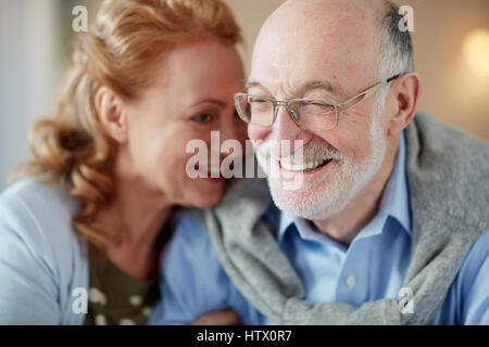 Porträt von senior Liebespaar sitzen eng zusammen kuscheln liebevoll lächelnd zu Hause im Mittelpunkt und älteren Mannes mit Brille Stockfoto